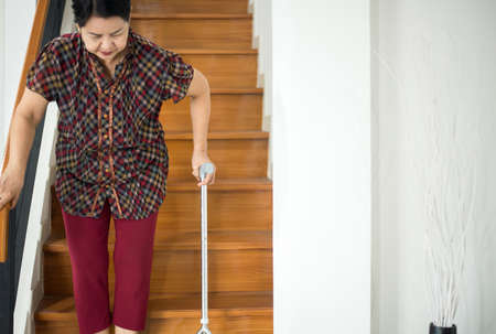 Elderly Asian woman holding sticks while walking down stair at homeの写真素材