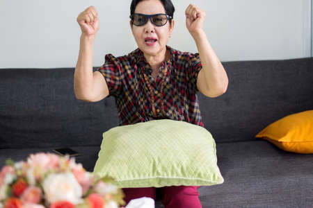 Happy senior Asian woman watching television on the couch in the living room at home