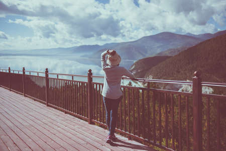 Happy and cheering woman stands with showing hands heart shape and looking beautiful while looking amazing mountains view at outdoorの写真素材