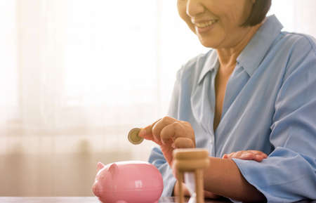 Asian senior hands putting coin to piggy bank for retirement,Saving money conceptの写真素材