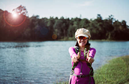 Backpacking Asian woman standing while looking camera at nature,Happy and smiling,Camping hiking conceptの写真素材