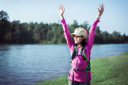 Backpacking Asian woman standing while looking something in the morning at outdoor,Happy and smiling,Camping hiking conceptの写真素材