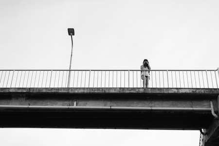 Depressed asian woman standing on overpass near railway at train station. Negative attitude. Black and white tonedの写真素材
