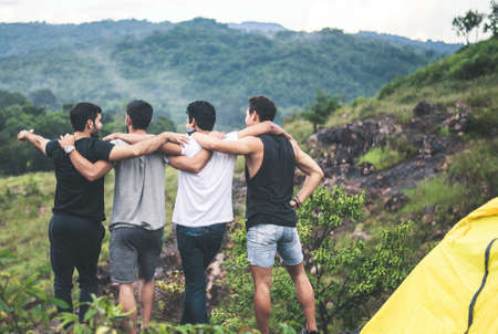 Cheerful young  man traveler friends hugging with hands raise up together at nature,Enjoying backpacking concept,Back viewの写真素材