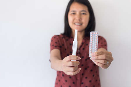 Happy asian woman hands holding birth control pill and pregnancy test,Concept for contraceptive,Copy space for text on white backgroundの写真素材