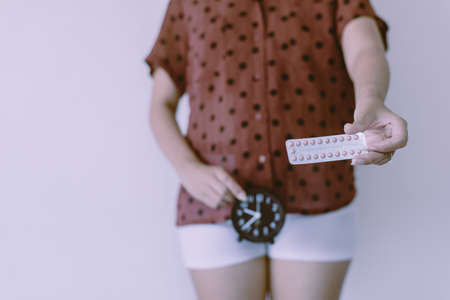 Woman hands holding birth control pill and clock,Concept for contraceptive,Copy space for text on white background,Close upの写真素材