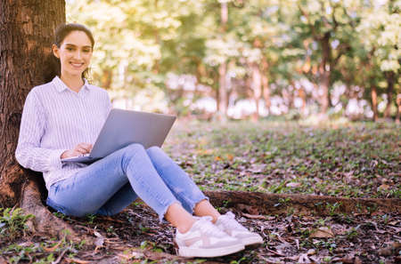 Beautiful young woman using laptop computer at park in the morning,Happy and smiling