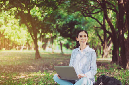 Beautiful young woman using laptop computer at public park in the morning,Happy and smiling,Relaxing...