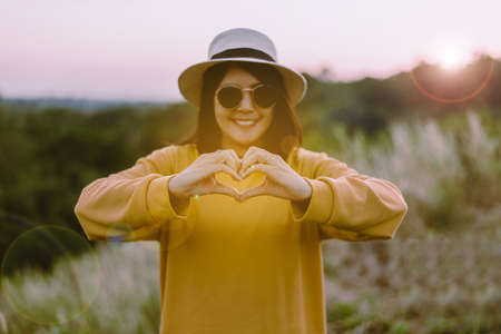Hipster young asian woman showing hands heart shape at sunset,Happy and smiling,Positive thinkingの写真素材