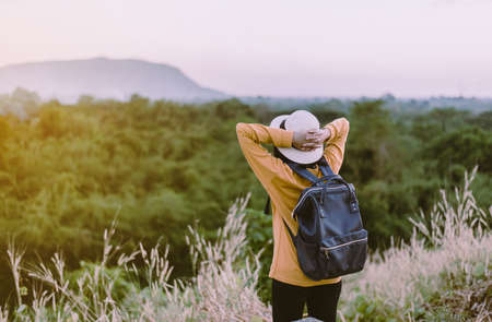 Hipster young asian woman standing and hands raise up at sunset,Happy and smiling,Positive thinking,Overcoming obstacle concept,Back viewの写真素材