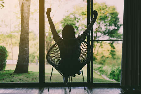 Woman sitting with hands raise up on modern chair in living room,Relaxing time,Happy and smiling,Back viewの写真素材