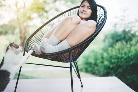 Beautiful young asian woman sitting with white cat on modern chair at nuture,Relaxing time,Happy and smilingの写真素材