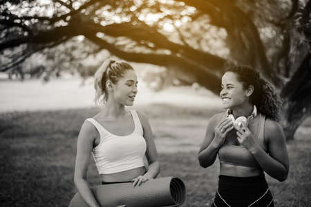 Couple of young sporty woman holding yoga mats and talking together at public park in the morning,Happy and smiling,Relaxing time,Black and white tonedの写真素材