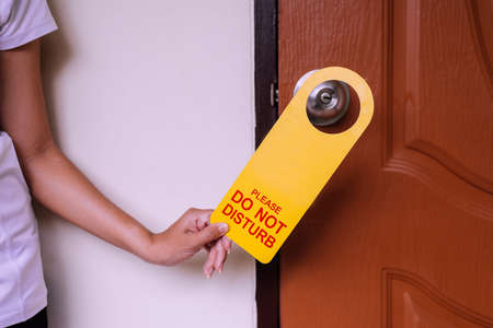 Woman hands putting closed door with please do not disturb sign on handle at hotel room