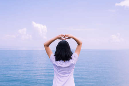 Happy young asian woman standing and showing 2 fingers at sea,Enjoying in Nature, Freedom concept, Back viewの写真素材