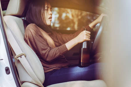 Drunk asian woman drinking alcohol while driving car on road,Women drives her car with a bottle of beer,Dangerous driving conceptの写真素材