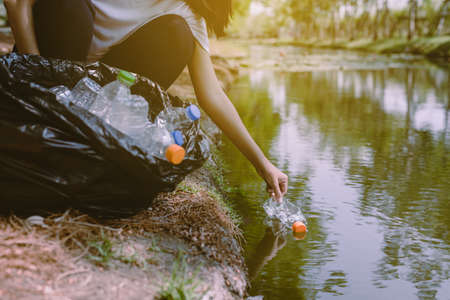 Woman volunteer picking up a bottle plastic trash from river,Environment and pollution campaign...