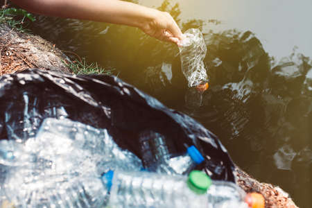 Woman volunteer hand picking up a bottle plastic trash in river,Environment and pollution campaign conceptの写真素材