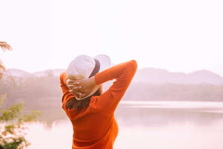 Happy woman standing and hands raise up at sunset,Happy and smiling,Positive thinking,Free time,Back viewの写真素材