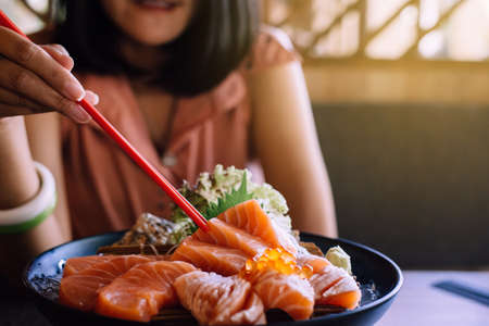 Hands woman using chopstick with raw salmon fillet and salmon roe Ikura on dish in restaurant,Japanese foodの写真素材