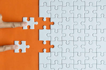 Woman hands putting Jigsaw puzzles,Jigsaw white color,Puzzle pieces grid,Success mosaic solution template,Concept of teamwork and businessの写真素材