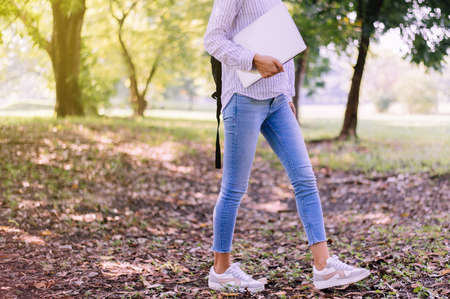 Happy young student woman holding laptop computer at public park in the morning,End of...