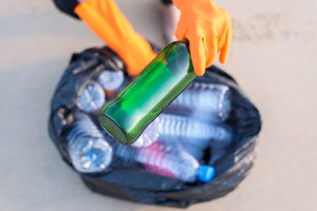 Volunteer hands holding black color garbage bag with keeping glass bottle at beach,Dispose recycle...