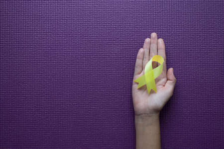 Woman hand holding yellow ribbon on purple background,