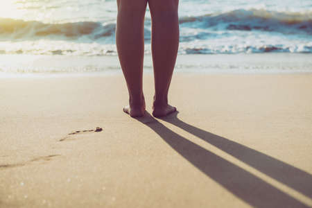 Close up of barefoot woman standing on the beach during sunset time,Vacation and holiday concept