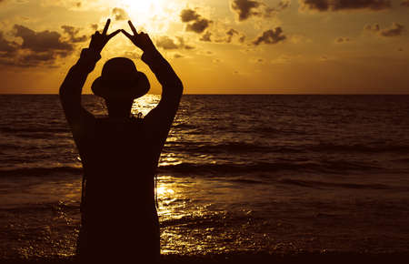 Silhouette of Happy man standing with showing 2 fingers while sunset at sea,Light flare,Enjoys of...