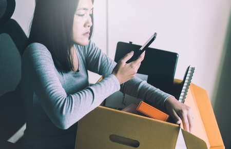 Woman using mobile phone and holding box equipment from work,Unemployment job conceptの写真素材