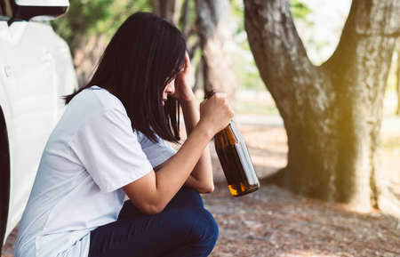 Drunk asian woman drinking alcohol while driving car on road,Women drive her car with a bottle of beer,Dangerous driving conceptの写真素材