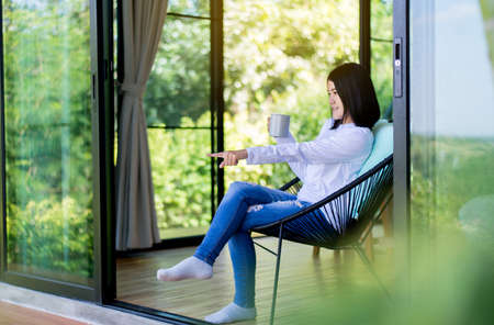 Happy asian woman drinking hot coffee and hand pointing something in bedroom at home,Coffee break,Take a break,Relax timeの写真素材