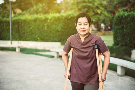 Patient mature asian woman using crutches support broken legs for walking at outdoor,Physical therapy conceptの写真素材