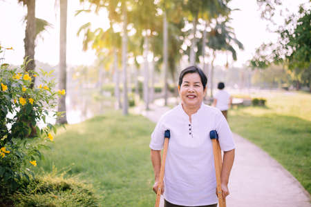 Patient mature asian woman using crutches support broken legs for walking at outdoor,Physical therapy conceptの写真素材