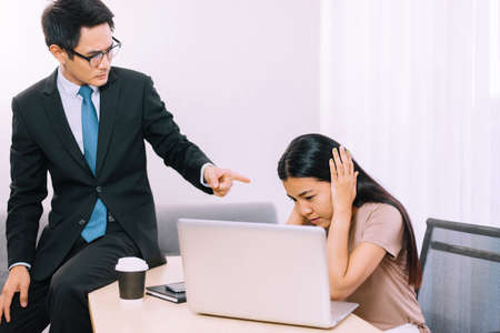 Asian man boss pointing finger to stressed woman employee in officeの写真素材