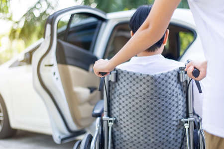 Caregiver helping senior handicapped asian woman from wheelchair get into carの写真素材