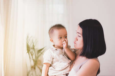 Adorable asian baby boy sucking thumb with mom carrying in bedroom,Happy new born kidの写真素材