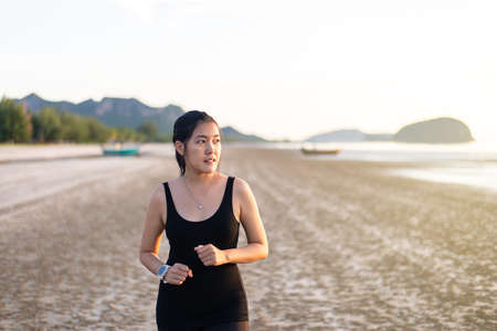 Fit asian woman running on the beach during sunset time