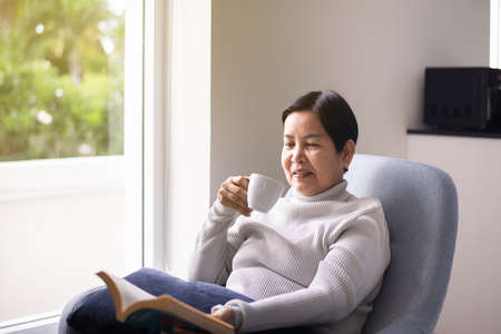 Elderly asian woman drinking coffee in living room at home,Happy and smiling,Relaxing time,Health care senior insurance conceptの写真素材