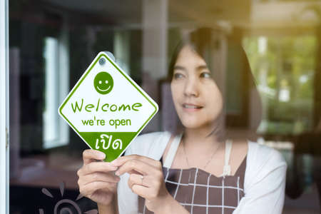Happy asian woman owner turning open sign after lockdown quarantine in modern cafeの写真素材