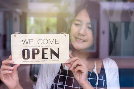 Happy asian women owner turning open sign after lockdown quarantine in modern coffee shopの写真素材
