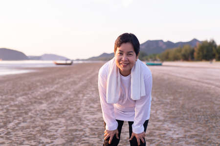 Happy elderly asian woman break and relax after workout at the beach in the morningの写真素材