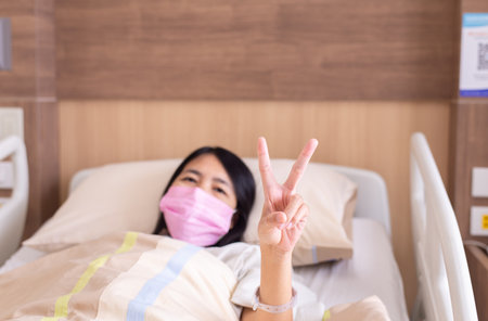 Patient Asian woman showing 2 fingers on sick bed at the hospitalの写真素材