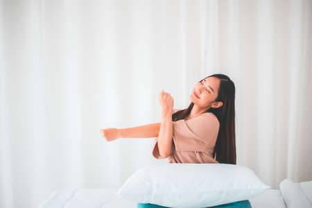 Happy young asian woman stretching and waking up in her bedroom at home in the morningの写真素材