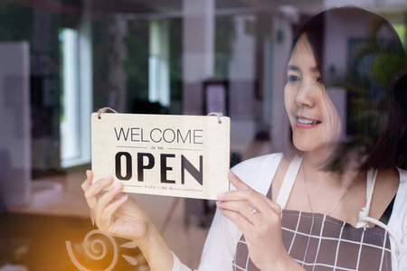 Happy asian woman owner turning open sign after lockdown quarantine in modern coffee shop,Reopeningの写真素材