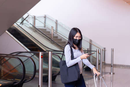 Asian woman wearing face mask and using mobile phone during coronavirus pandemic in the mallの写真素材