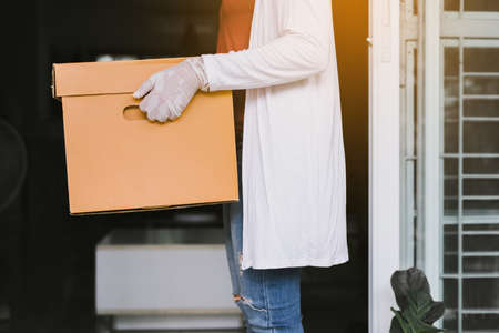 Woman hands holding paper box from delivery service during virus pandemic situation at homeの写真素材