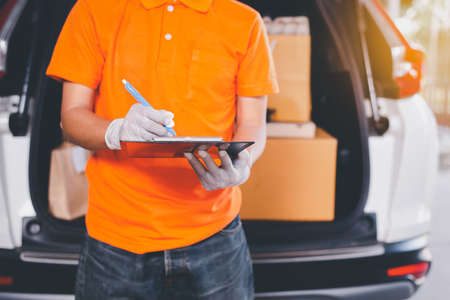 Delivery man employee checking list on clipboard standing in front of van during pandemic situation
