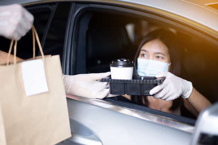Food delivery courier give coffee cup to woman in her car,Safety food during coronavirus pandemic situationの写真素材